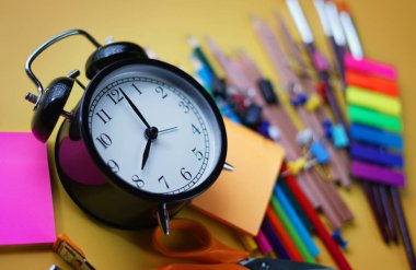 Çalar saat ve sarı zemin üzerine okul kırtasiye