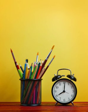 Çalar saat ve okul sabit sepeti ahşap masa üzerinde sarı arka plan