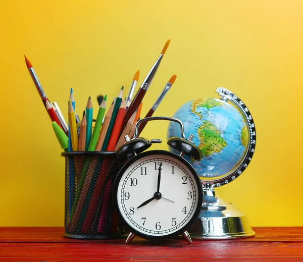 Alarm Clock, World Globe and School Stationary in Basket on Wooden Table Yellow Background