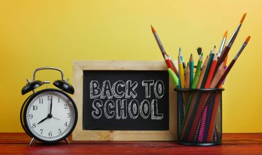 Okul metne geri. Çalar saat, Blackboard ve okul sabit sepeti ahşap masa üzerinde sarı arka plan