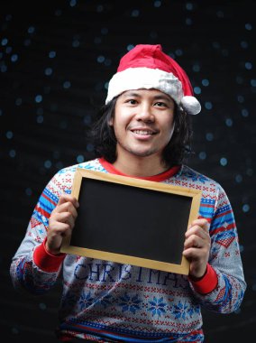 Asya adam Noel Baba şapkası ve Blackboard tutan Noel kazağı giymiş