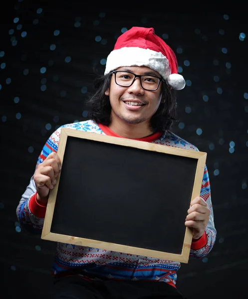 亚洲男子身穿圣诞老人帽和圣诞毛衣持有黑板 — 图库照片