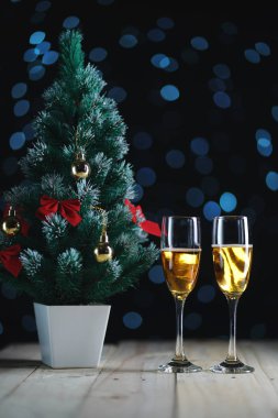 İki kadeh şampanya ve küçük Noel ağacı koyu parlayan ışıklar arka plan.