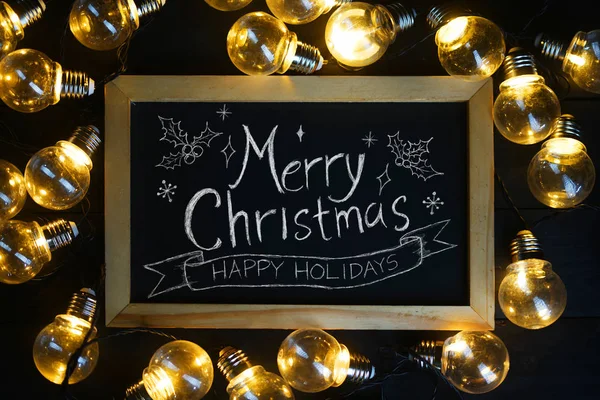圣诞快乐 在黑色木材上的灯泡之间的黑板上的圣诞彩印 — 图库照片