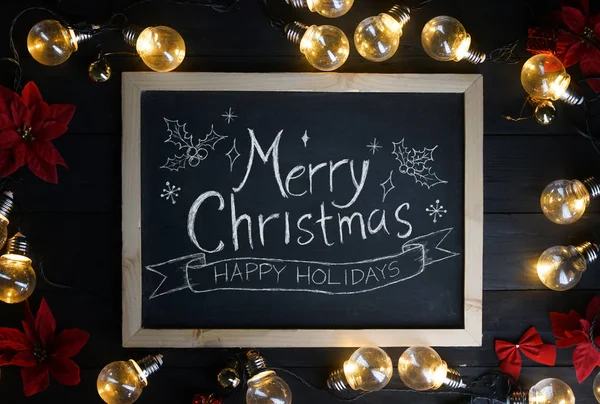 圣诞快乐 在灯泡和黑色木材上的红色指针之间的黑板上的圣诞彩印 — 图库照片