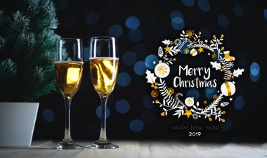 Mutlu Noeller Tipografi sanat. İki kadeh şampanya ve küçük Noel ağacı koyu parlayan ışıklar arka plan.