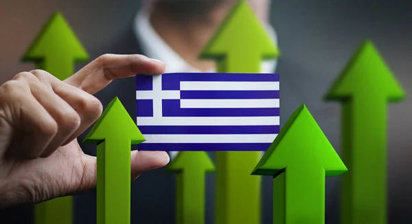 Nation Growth Concept, Green Up Arrows - Businessman Holding Card of Greece Flag