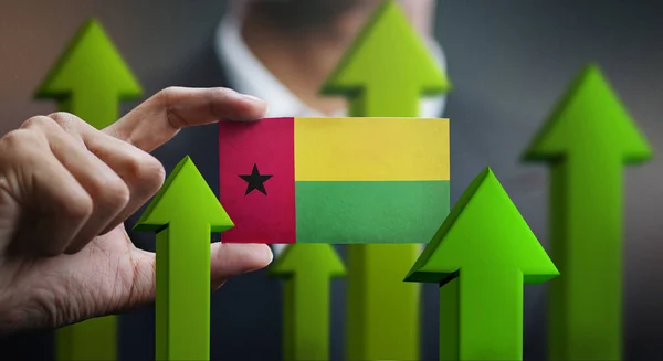 Nation Growth Concept, Green Up Arrows - Businessman Holding Card of Guinea-Bissau Flag
