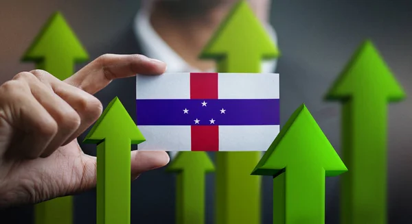 Nation Growth Concept, Green Up Arrows - Businessman Holding Card of Netherlands Antilles Flag