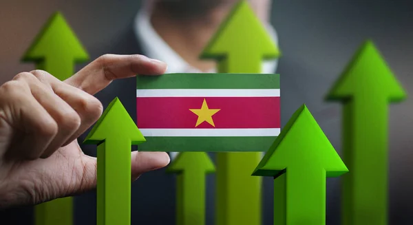 Nation Growth Concept, Green Up Arrows - Businessman Holding Card of Suriname Flag