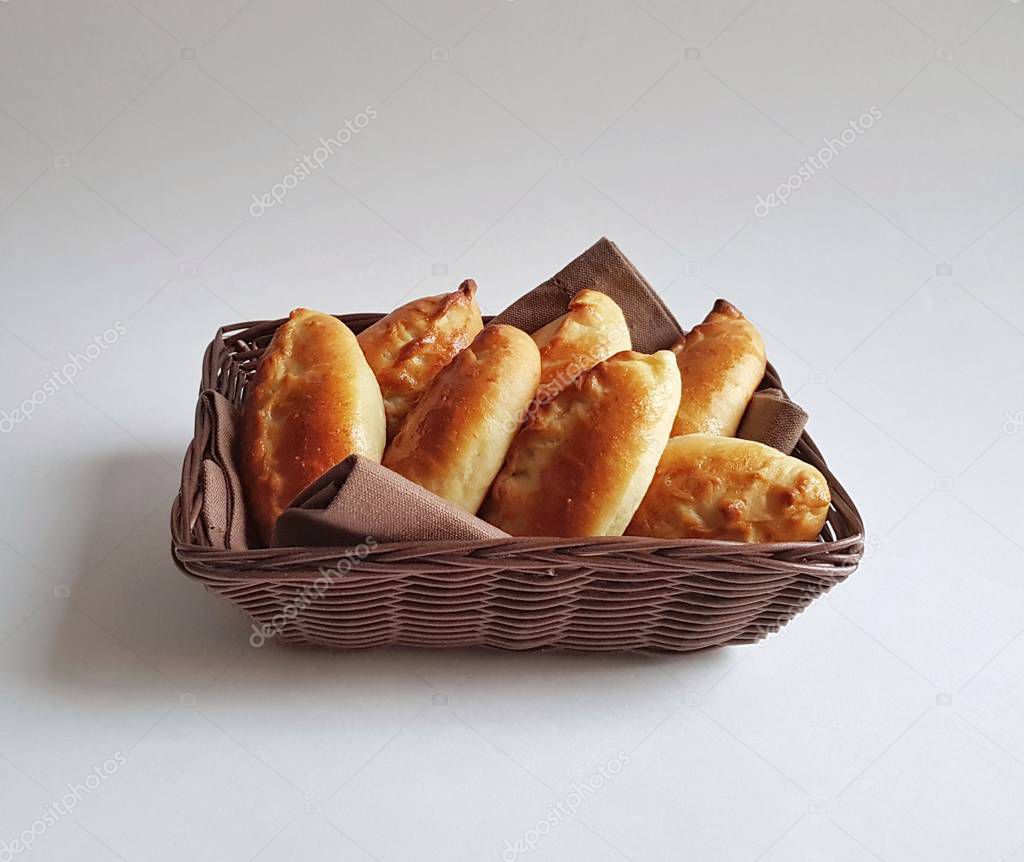 Traditional Russian baked pies pirozhki (patties) in a basket. Ruddy yeast buns with a golden crust. White background. isolated. Pies can be cooked with cabbage, apples, eggs, berries, fruit, meat