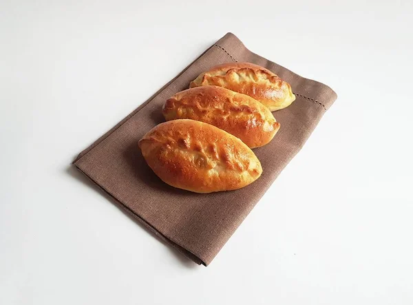 Geleneksel Rus pirozhki turtaları (köfteler) kahverengi bir peçetenin üzerinde. Beyaz arka plan. İzole. Turtalar lahana, elma, yumurta, dut, meyve ve etle pişirilebilir.