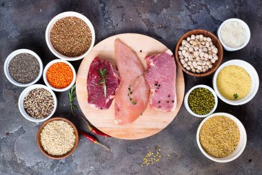 Çiğ gıda sığır eti ve tavuk göğsü ile hububat kase taş koyu arka plan üzerinde düz yatıyordu. Dengeli beslenme, yemek, mutfak ve gıda kavramı