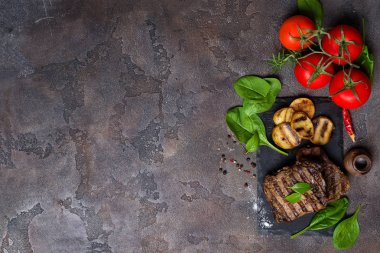Lezzetli sığır eti biftek ve ızgara sebzeler, domates, ıspanak taş masada kayrak gemide. . Kopya alanı ile üstten görünüm