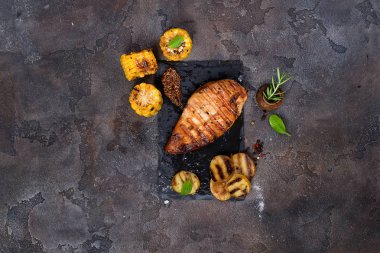 Terbiye edilmiş ızgara sağlıklı tavuk göğsü yaz barbeküsünde pişirilir ve taş zeminde taze otlar, patatesler ve mısırla servis edilir.