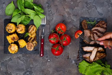 bir çatalla dilim tomat ıspanak, domates ve kopya alanı, düz taş zemin üzerine ızgara patates ile kayrak plaka üzerinde ızgara biftek taze üç tür arka plan üzerinde yatıyordu el tutar