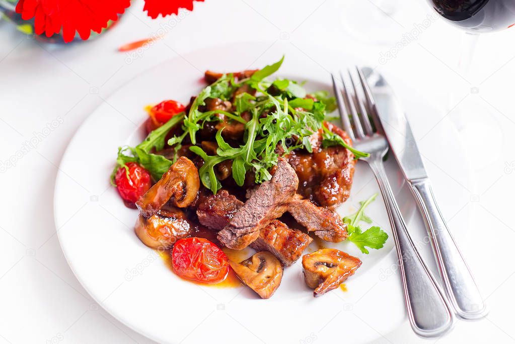 Juicy steak medium rare beef with spices and grilled vegetables with salad on a white plate on a textile background with red wine