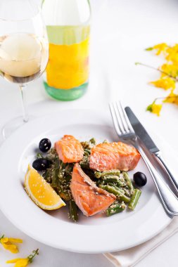 Haşlanmış yeşil fasulye ve beyaz şarap ve çiçeklerle masada beyaz tabak içinde limon ile ızgara somon