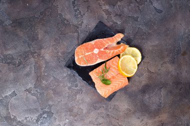 Taş kesme tahtası üzerinde biberiye ve limon dilimi ile çiğ somon fileto. Yağsız protein.