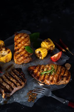 Üç çeşit kağıt üzerinde karanlık bir arka plan üzerinde ızgara et tavuk, domuz eti ve domates ve Mısır ile sığır eti, baharat. Düz yatıyordu