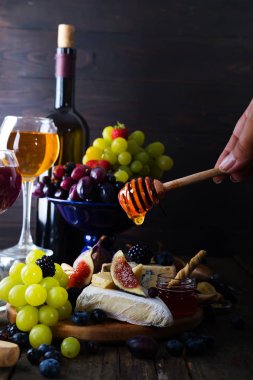Üzüm, peynir, incir ve onun kırmızı ve beyaz tahta bir arka plan üzerinde şarap bir bardak ballı bir sopayla el.