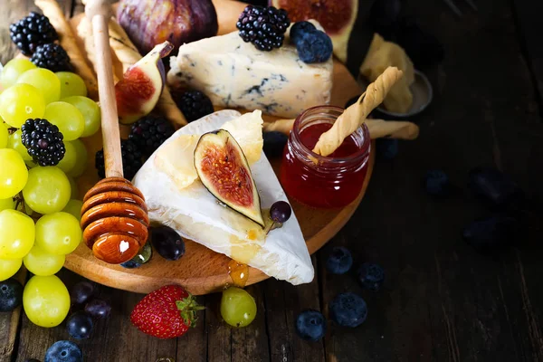 Üzüm, peynir, incir ve sopa ile kırmızı ve beyaz tahta bir arka plan üzerinde şarap bir bardak ballı.