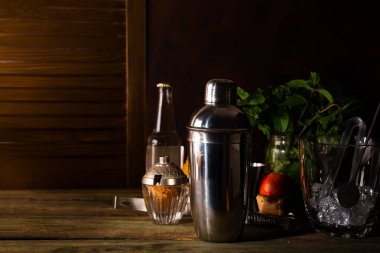 Kokteyl shaker, karıştırma, maşa ve kaşık bir kova buz ile kopya alanı ile koyu ahşap bir masa üzerinde bir yaz kokteyl içecek hazırlama