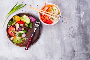 Domates, portakal, ceviz, salata ve salatalık, turp Çin eriştesi ve havuç üzerine taş arka plan düz lay ile sağlıklı salata tabağı. Gıda ve sağlık. Temiz yemek.