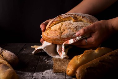 Rustik organik somun ekmek tutan eller - kırsal ekmek fırıncı kadın. Pişirme ve pişirme kavramı arka plan. Baker ellerin dikkatle somun ahşap masa un serpilir, bir dakika.