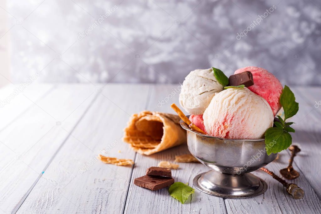 Trio of tasty vanilla and strawberry flavored frozen dessert in a bowl with wafer straws and ice berries on wooden background
