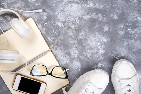 Top view of travel stuff. Essential travel items. shoes, smart phone, camera, notebook, headphones and sun glasses on stone gray table background, copy space. Flat lay