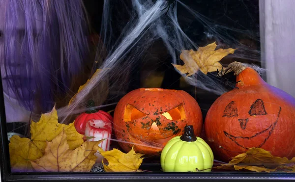 Scary halloween pumpkins placed in front of window with scary background mystical house window with rain drope and spider web, and a ghost face in the background