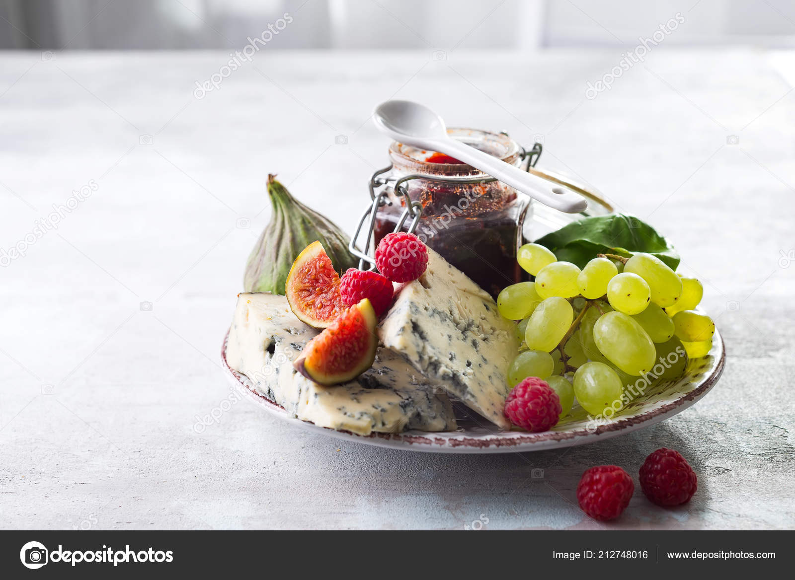 Delicacy blue cheeses, fruit and jam in jar on white stone background