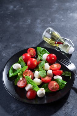 Olgun kiraz domates ile lezzetli caprese salatası ve mini mozzarella peynir topları Taze Fesleğenli siyah saç ve koyu arduvaz arka plan üzerinde bırakır. İtalyan sağlıklı gıda kavramı