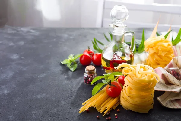 Pasta ingredienser. Körsbärstomater, spaghetti pasta, basilika och kryddor på tabellen sten över ett fönster — Stockfoto