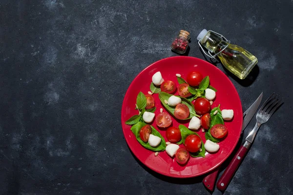 Fresh italian caprese salad with mozzarella and tomatoes on red plate over dark stone background with copy space, flat lay — 图库照片