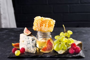 Üzüm, peynir, incir ve bal bir taş üzerinde siyah arka plan üzerinde siyah tuğla duvar, kopya alanı