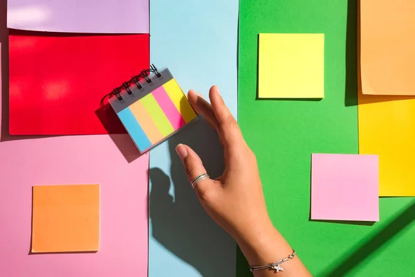 Разноцветная бумага стек на спирали, как радуга с женской рукой на цветном бумажном фоне, вид сверху. Концепция исследования, бизнес для заметок — стоковое фото