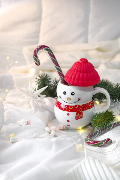 Couverture douce confortable avec une tasse sous la forme d'un bonhomme de neige avec des bonbons de Noël sur le lit avec des lampes de poche. Concept de Noël matin paresseux, ambiance hivernale chaude — Photo