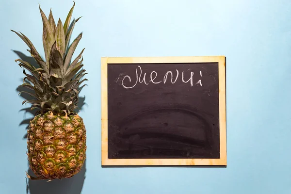 slate chalk board template menu with pineapple on blue paper background, flat lay with copy space