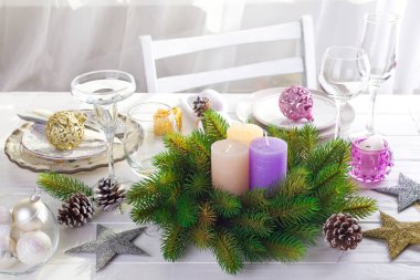 Beyaz ahşap bir masa ışık pencerenin önünde bir Noel tablo ayarı ile bir tablo üzerinde renkli büyük mumlar ile Noel çelenk