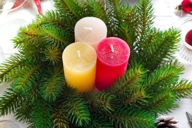 Noel sofrasında mum, fener, sofra takımı ve şarap kadehleriyle beyaz ahşap arka planda şölen dekorasyonu.