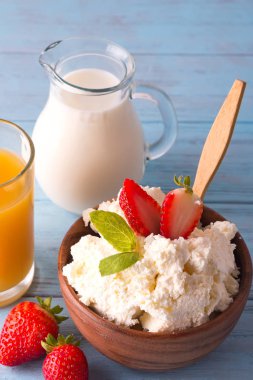 Bir kaşık, bardak süt, eski ahşap bir zemin üzerine suyu kavanoz ahşap bir kase çilek taze süzme peynir. Kavram sağlıklı kahvaltı
