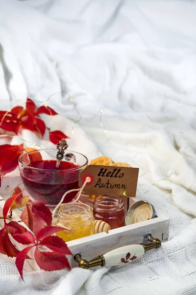 Herbstliches Herbstkonzept mit Strickdecke und heißem Tee mit Watte, Marmelade, Honig auf Holztablett auf dem Bett, Herbstblatt und Kerze. Kopierraum — Stockfoto
