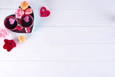 İki bardak kahve, beyaz bir arka plan üzerinde bir kalp şeklinde bir kutu içinde çiçekli macaroons. Sevgililer günü kavramı, düz kopya alanı ile yatıyordu