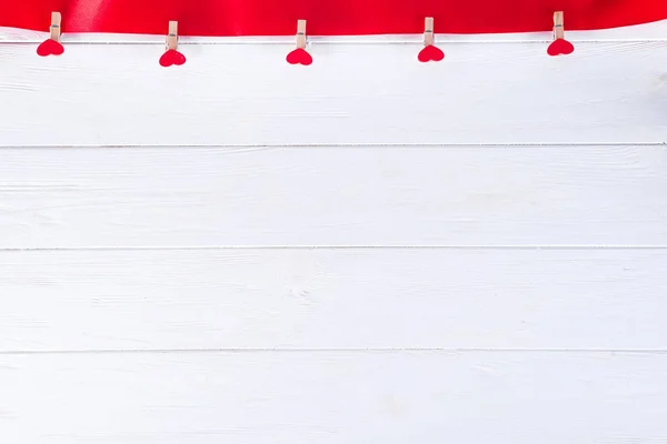 Pinzas de ropa con corazones rojos en una cinta roja como un borde sobre un fondo de madera blanca con espacio para el texto. El concepto de San Valentín, espacio para copiar — Foto de Stock