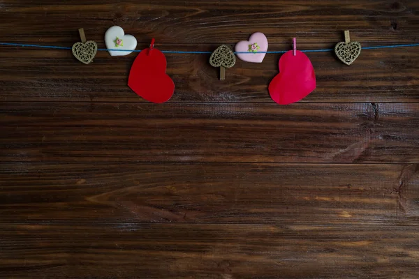 Clothespins com corações vermelhos em uma fita como uma borda em um fundo de madeira marrom com espaço para o texto. O conceito de Dia dos Namorados, espaço de cópia — Fotografia de Stock