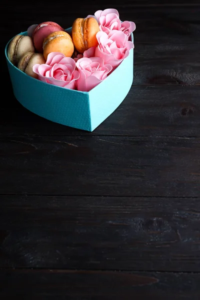 Macaron in scatola. Scatola blu rotonda festiva con biscotti e rosa su sfondo di legno scuro, copia lo spazio — Foto Stock