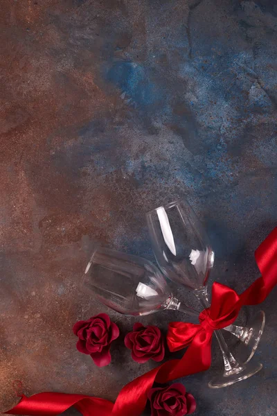 Фон празднования Дня Святого Валентина с двумя стаканами, розами и красной лентой на каменном фоне с копировальным пространством, плоский лежал . — стоковое фото
