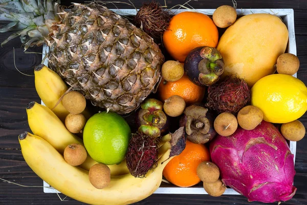 Fresh exotic fruits in a wooden box, top view with many colorful ripe fruits